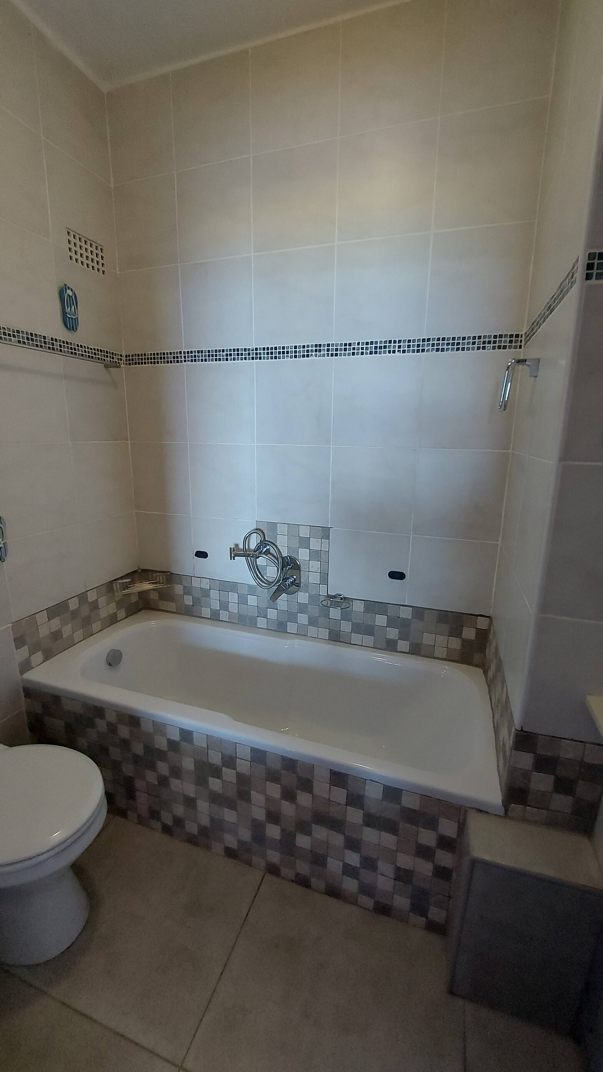 A bathroom with a bathtub, toilet, and tiled walls.