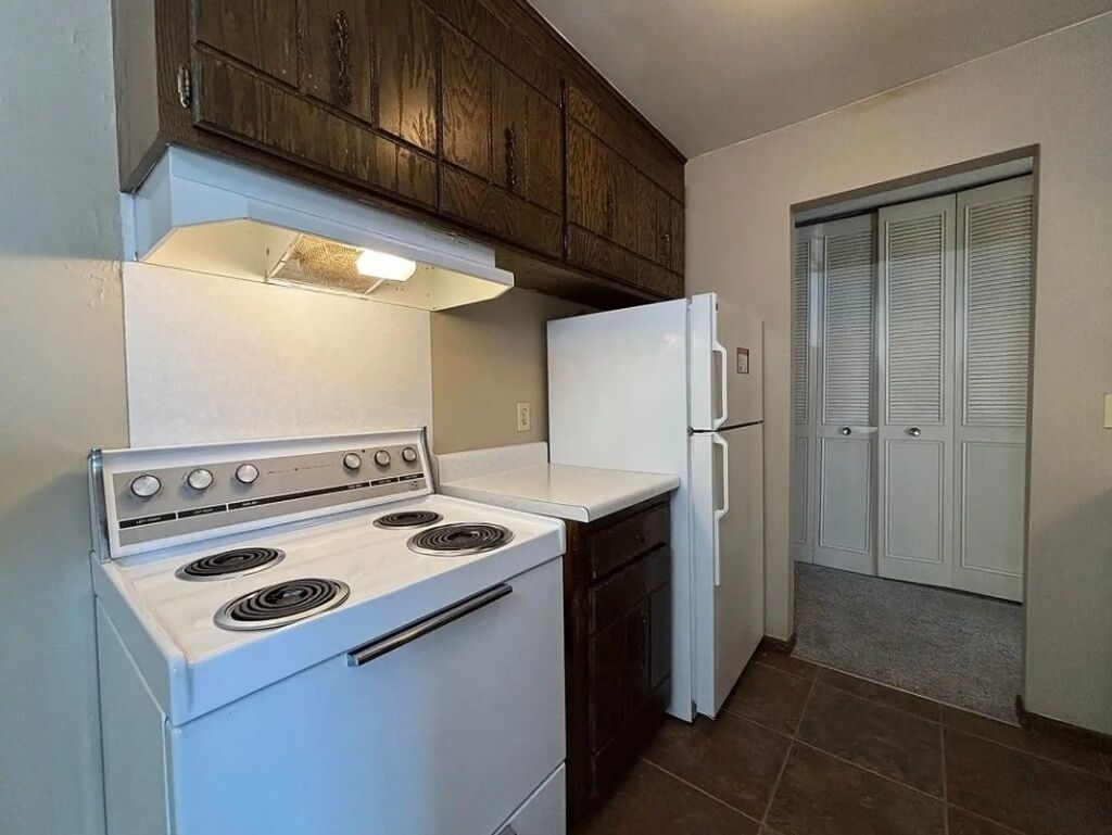 A kitchen with a white stove, a white refrigerator, and wooden cabinets.