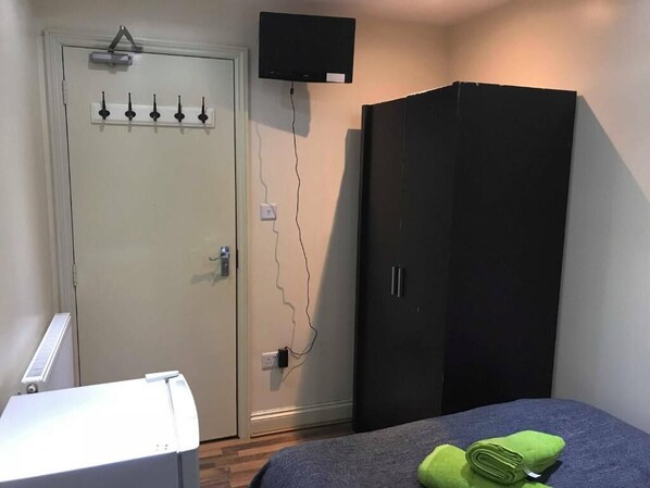 A bedroom with a bed, a wardrobe, a television mounted above the door, and a radiator.