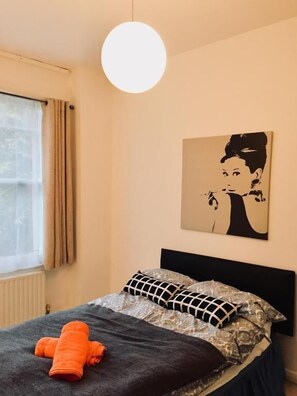 Een slaapkamer met een bed, een hanglamp, een raam met gordijnen en een kunstwerk aan de muur.