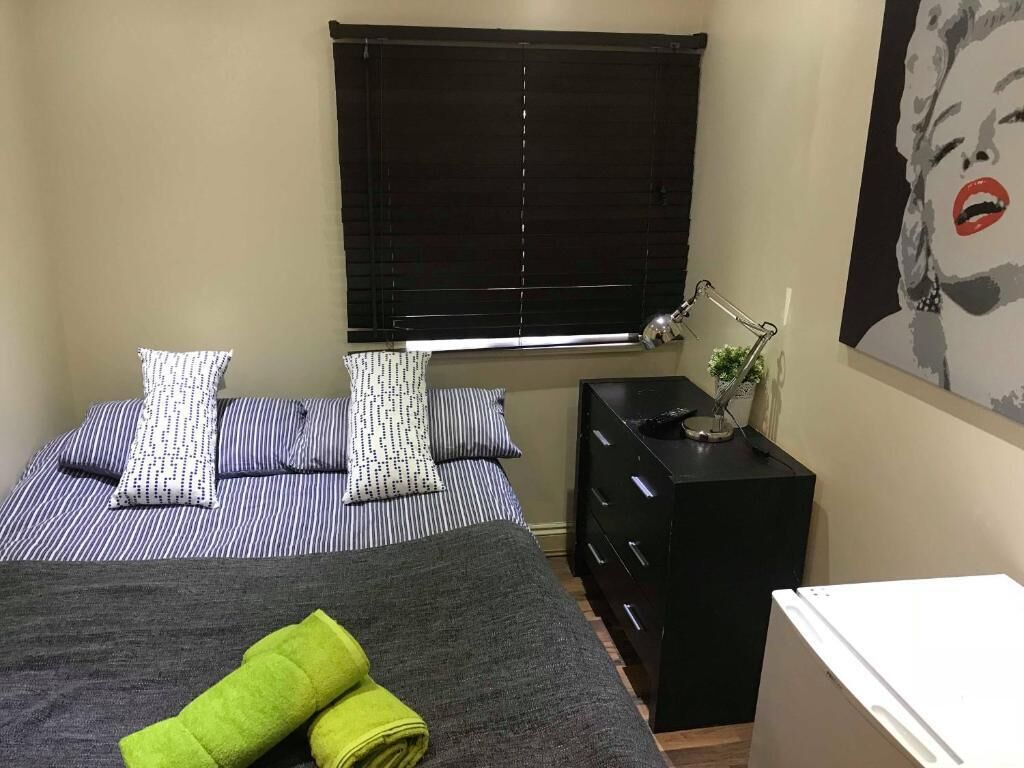 Une chambre à coucher avec un lit, des oreillers, une table de chevet avec une lampe, une commode et un tableau au mur.