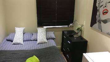 Une chambre à coucher avec un lit, des oreillers, une table de chevet avec une lampe, une commode et un tableau au mur.