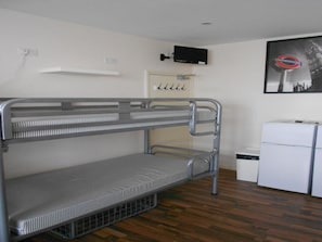 Habitación con literas, una pequeña kitchenette, un televisor montado en la pared y un cartel de un tema subterráneo.