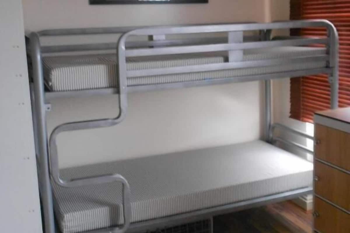 A bunk bed with metal railings, a small wooden dresser, and a framed picture on the wall.