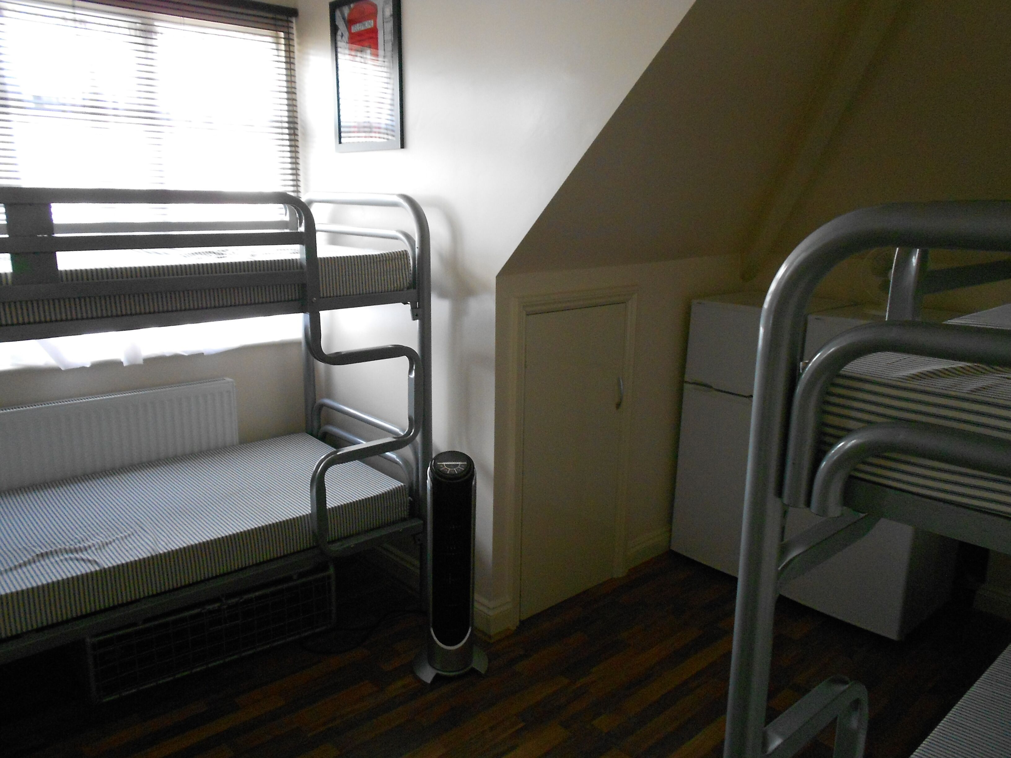 A dormitory room with bunk beds, a radiator, a heater, and a window with blinds.