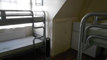 A dormitory room with bunk beds, a radiator, a heater, and a window with blinds.