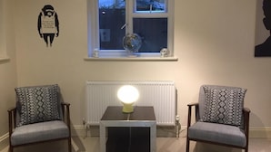 A room with two armchairs, a table with a lamp, a window with a globe, and a radiator. - Mapesbury Hostel (London)