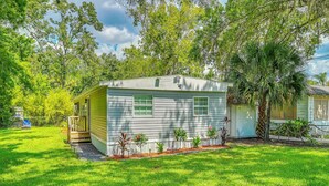 A single-story mobile home with a front porch, surrounded by a well-maintained lawn and various trees. - Weeki Wachee Springs Gem: Relax and Explore (Spring Hill)