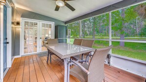 A covered outdoor area with a table and chairs, a ceiling fan, and large windows offering a view of the outdoors. - Weeki Wachee Springs Gem: Relax and Explore (Spring Hill)
