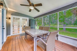 Ein überdachter Außenbereich mit Tisch und Stühlen, einem Deckenventilator und großen Fenstern mit Blick ins Freie.