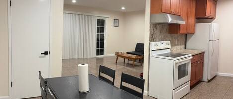 A compact kitchen with a stove, oven, and refrigerator, a dining table with chairs, and a sliding door leading to a living area.