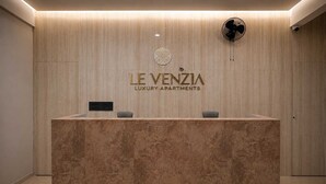 Un mostrador de recepción con encimera de mármol, un logotipo en la parte superior y un ventilador en la pared a la derecha.
