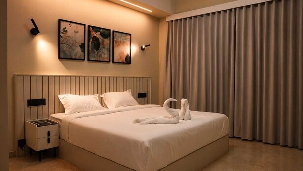 Una habitación de hotel con una cama grande, una mesita de noche, una lámpara de pared y una ventana con cortinas.