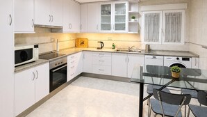 A modern kitchen with white cabinets, a microwave, stove, sink, and a glass dining table with chairs. - The tranquility of the Mediterranean, the comfort of a spacious apartment in Villajoyosa (La Vila Joiosa)