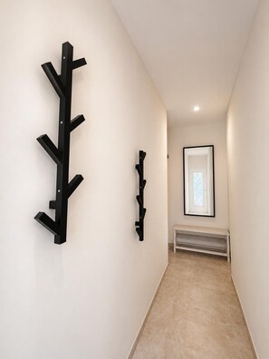 Ein Flur mit einem schwarzen Kleiderständer, einem kleineren, an der Wand befestigten Ablage und einem gerahmten Bild.