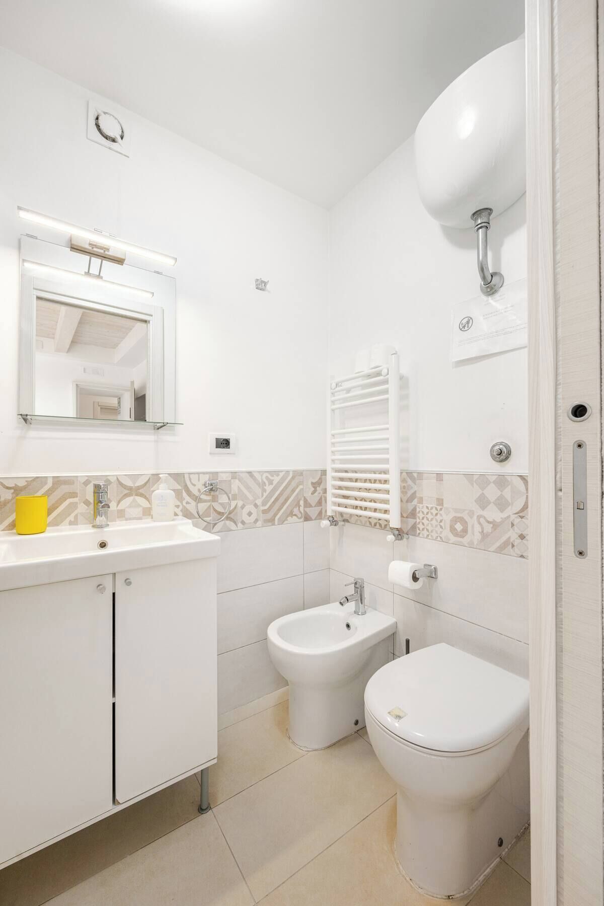 A bathroom with a white sink, bidet, toilet, and a towel rack.
