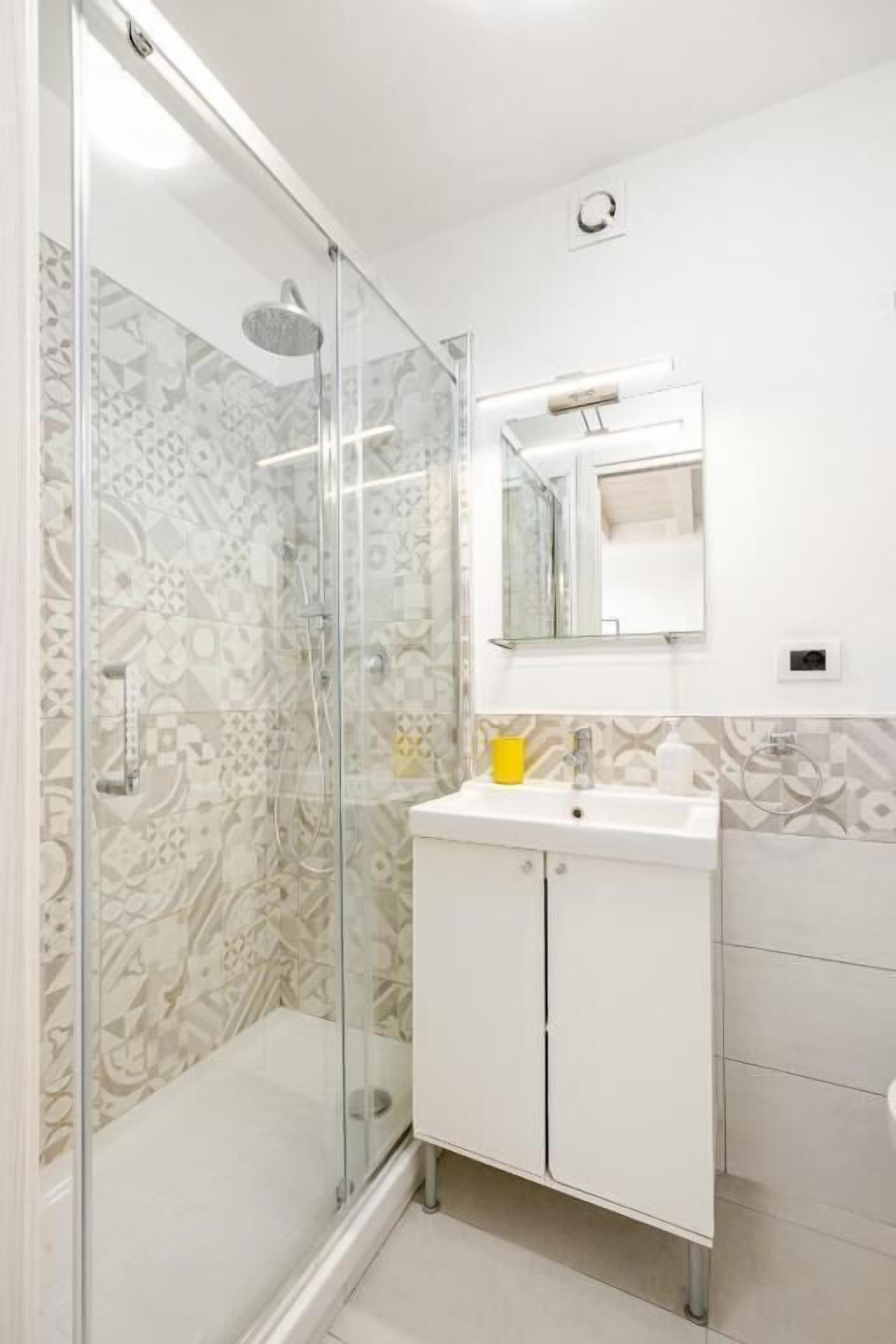 Un bagno con doccia vetrata, un lavandino bianco e uno specchio sopra.