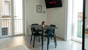 A room with a dining table, chairs, a TV mounted on the wall, and a window with a view. - NALUSA ROOMS IN CENTRO A TOLEDO (Naples)