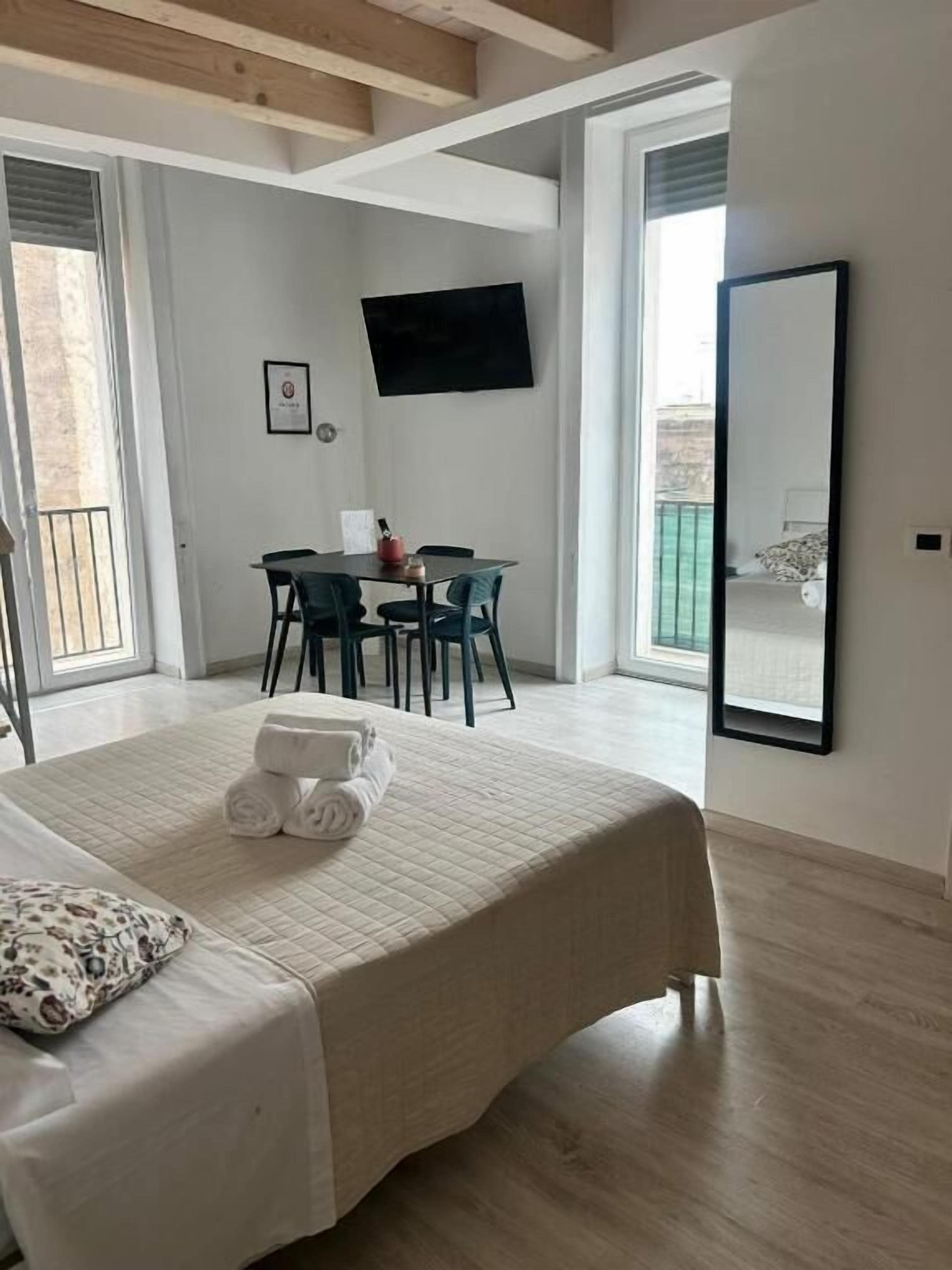 Habitación de hotel con cama, escritorio y silla. Hay un televisor en la pared y un espejo grande.