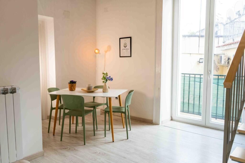 Un comedor con mesa y sillas, una lámpara fijada a la pared y un certificado enmarcado.