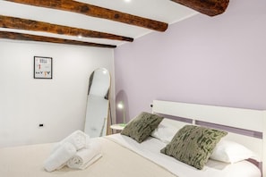 Quarto com cama, almofadas, espelho e um quadro na parede.