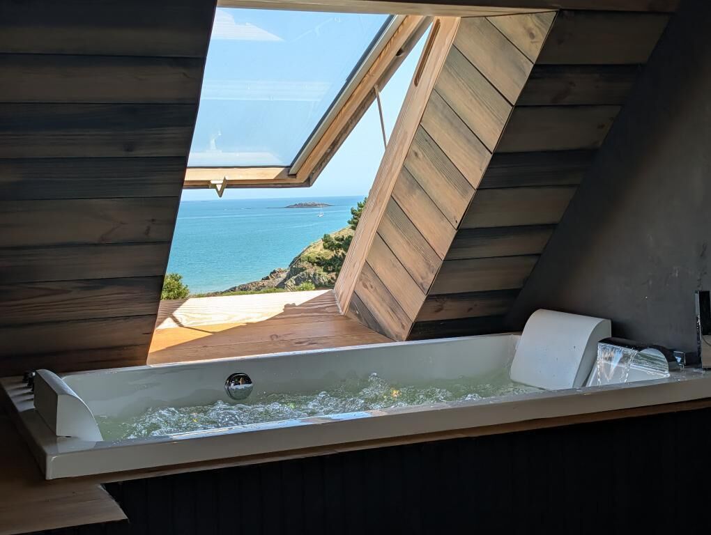 Een houten kamer met een dakraam, een badkuip en uitzicht op zee.