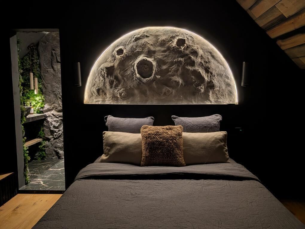 Een slaapkamer met een bed, kussens en een wanddecoratie in de vorm van een maan.