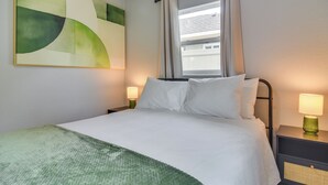 Ein Hotelzimmer mit einem Bett, zwei Nachttischlampen, einem Fenster mit Vorhängen und einem großen, abstrakten Gemälde an der Wand.