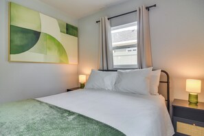 A hotel room with a bed, two bedside lamps, a window with curtains, and a large abstract painting on the wall. - 4 Mi to Beach! Dual-Unit Safety Harbor Retreat (Safety Harbor)