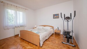 Ein Schlafzimmer mit einem hölzernen Bett, einem Nachttisch, einer Lampe, einem Fenster mit Vorhängen und einem stationären Heimtrainer.