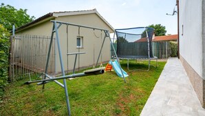 Ein Garten mit Schaukel, Trampolin und einer kleinen Rutsche.