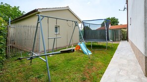 Ein Garten mit Schaukel, Trampolin und einer kleinen Rutsche.