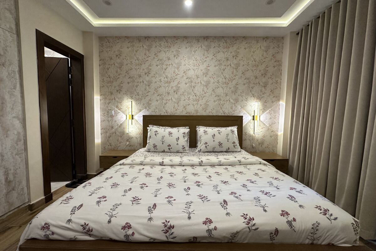 Un dormitorio con cama, ropa de cama estampada con motivos florales, dos lámparas de pared y una puerta.
