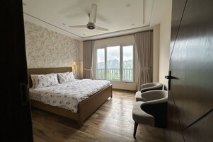 Un dormitorio con cama, una silla, ventilador de techo y ventana con cortinas.