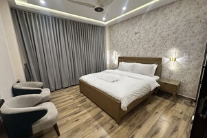 Un dormitorio moderno con una cama de madera, dos sillones, una mesita de noche y un ventanal con cortinas.