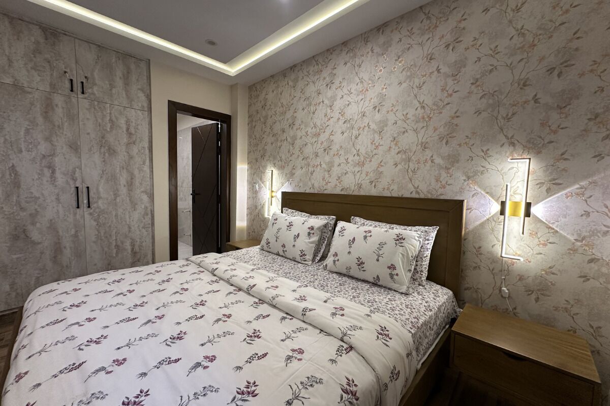 A bedroom with a bed, nightstands, a wardrobe, and a wall-mounted light fixture.