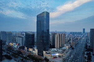 A high-rise building with a modern glass facade, surrounded by other high-rise buildings and a busy road with traffic.