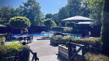Zona de piscina exterior con una fuente, rodeada de follaje y protegida por sombrillas.
