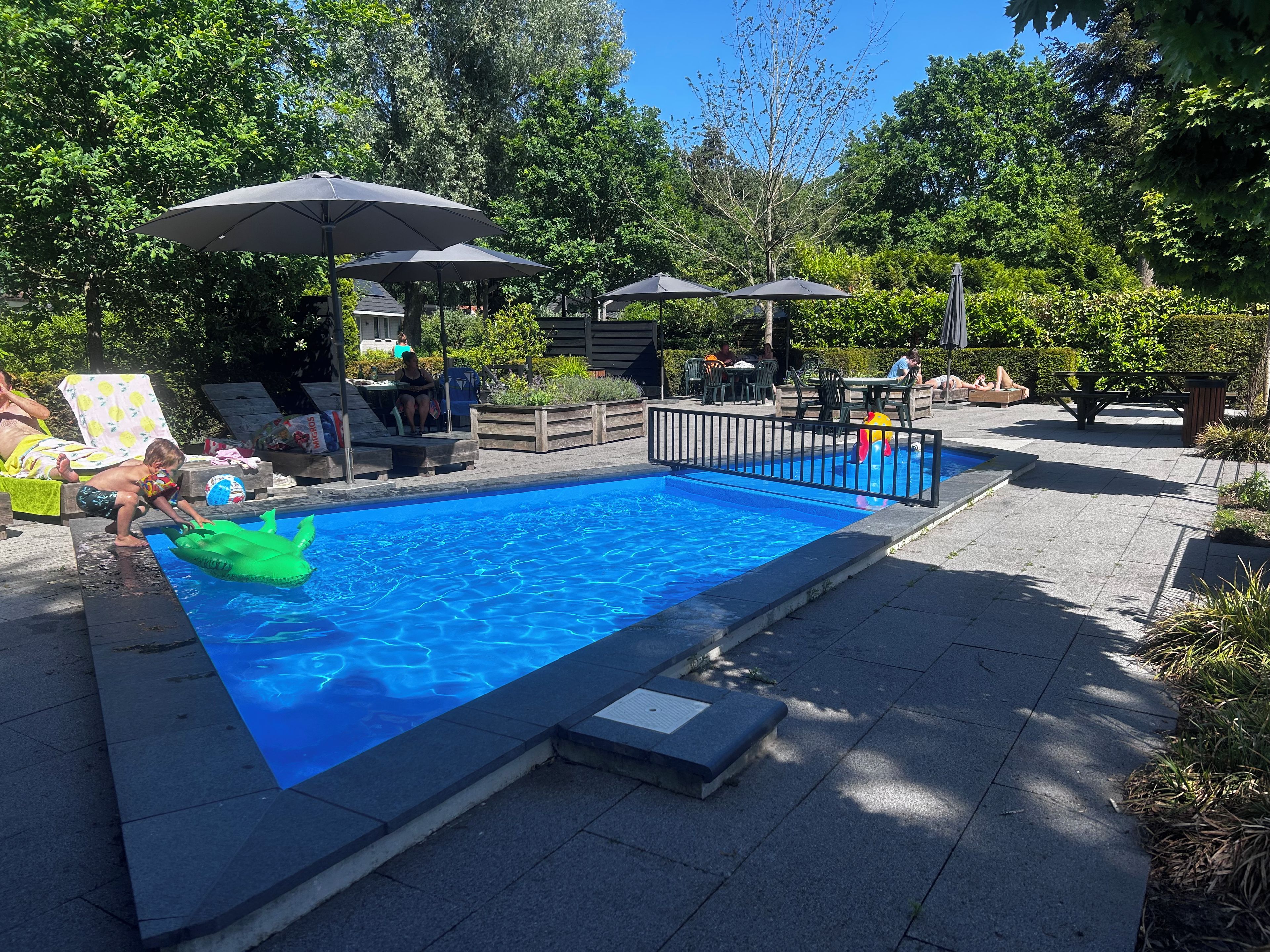 Une piscine avec une terrasse en bois, des chaises longues et des parasols.