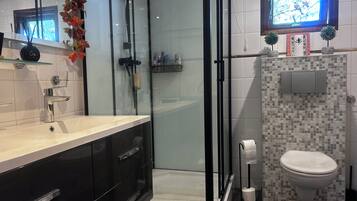 Une salle de bain moderne dotée d’une douche à parois de verre, de toilettes décorées de mosaïques et d’un meuble-lavabo avec des armoires noires.