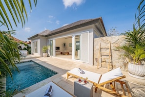 Una casa moderna con piscina, mobiliario exterior y un muro de piedra.
