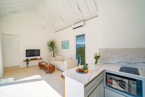A modern living room with a sofa, a coffee table, a TV, and a kitchen area with a marble countertop. - Calula Beach House II Uluwatu (Uluwatu)
