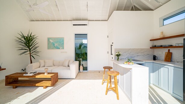 Um interior moderno com um sofá branco, mesa de centro de madeira e cozinha com bancadas de mármore.