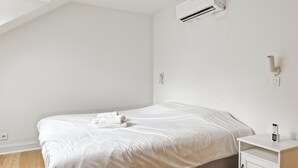 Et minimalistisk soveværelse med seng, natbord, klimaanlæg og vægmonteret lampe.