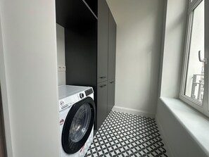 Ein kleiner Waschraum mit einer Frontlader-Waschmaschine, einem schwarzen Schrank und einem Musterboden.