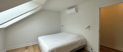 Une chambre avec un plafond en pente, un lit, un appareil de climatisation et une porte.