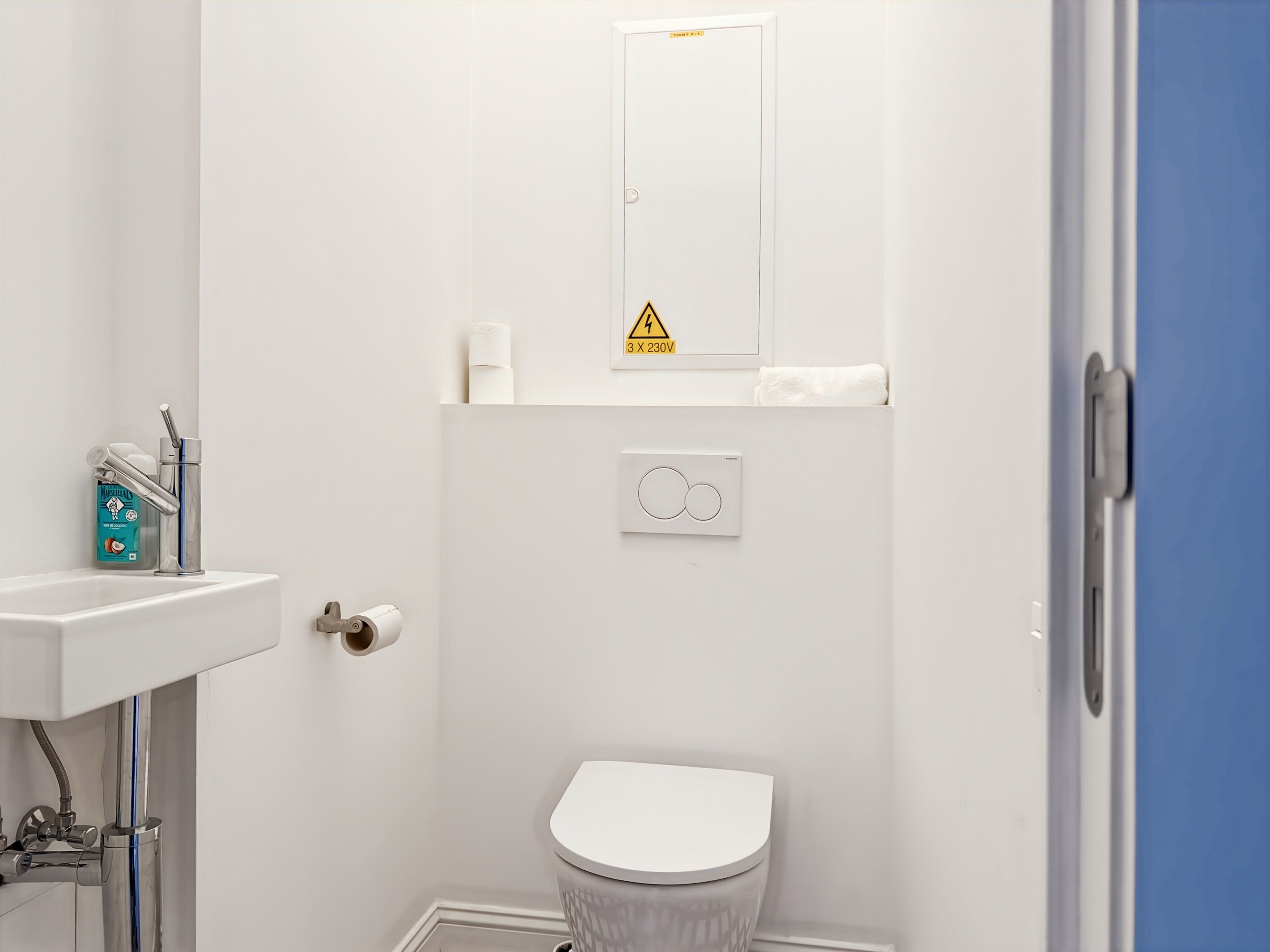 Ein Badezimmer mit Toilette, Waschbecken, Wasserhahn, Toilettenpapierhalter und Handtuchhalter.