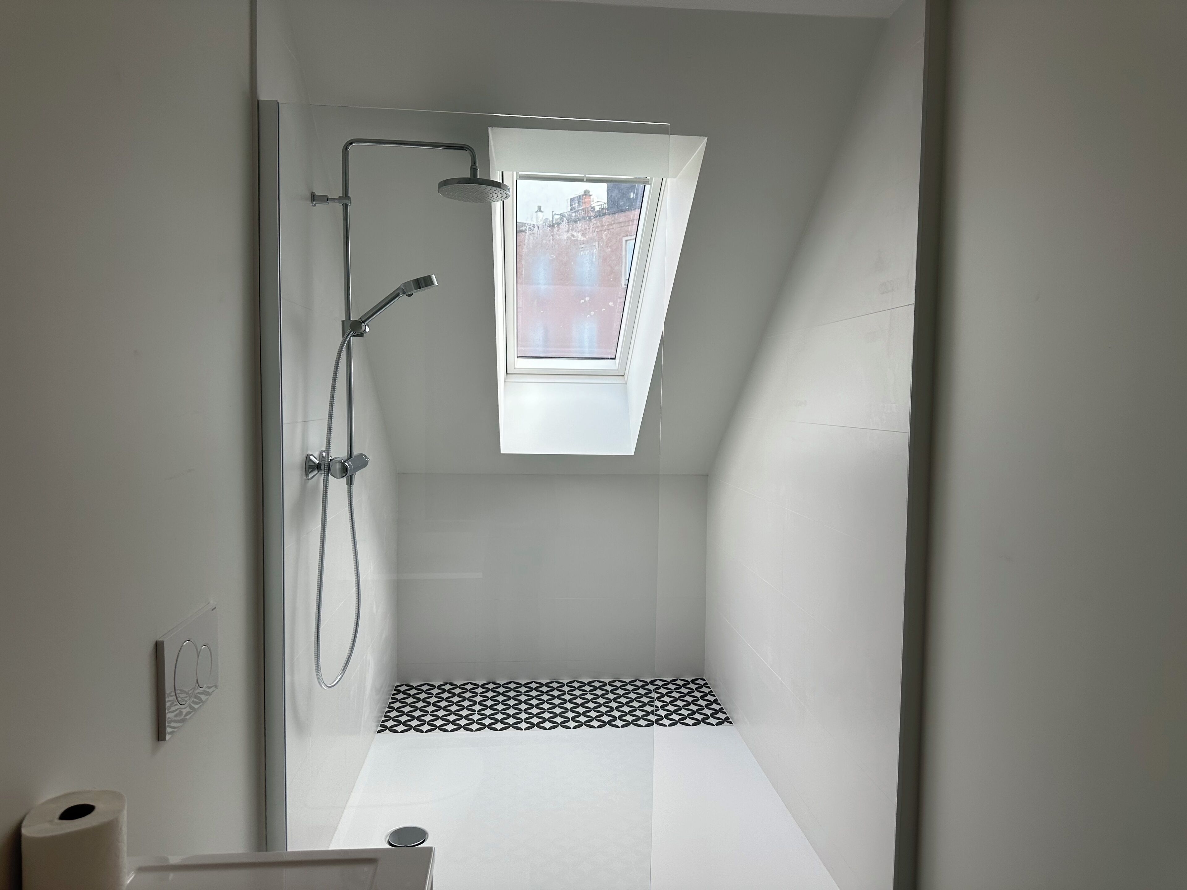 A modern shower with a skylight, white walls, and a geometric tile pattern on the floor.