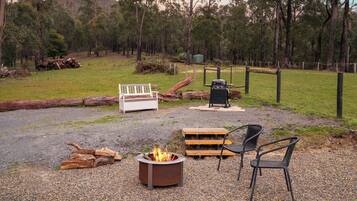 A gravel patio with a fire pit, a bench, a grill, and a chair.