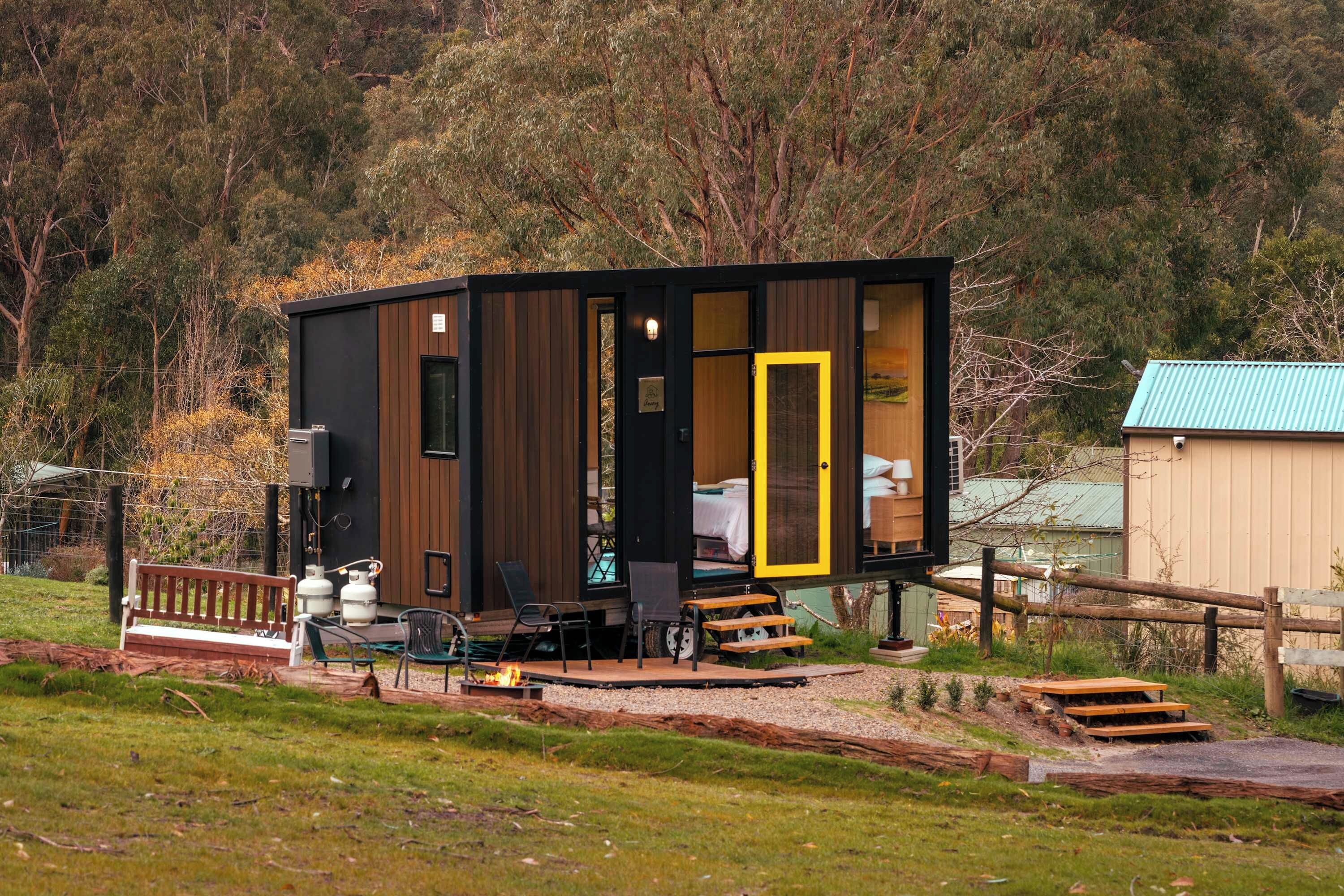 A cabin with a deck, outdoor seating, and a visible interior with a bed.